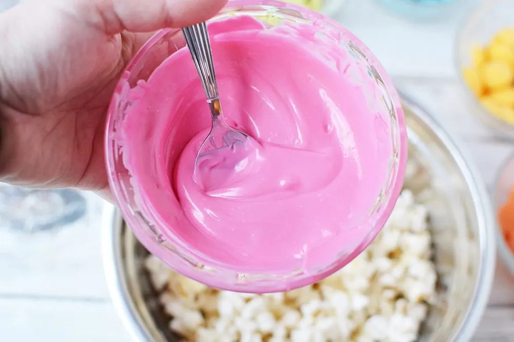 Pink candy melt above popcorn.