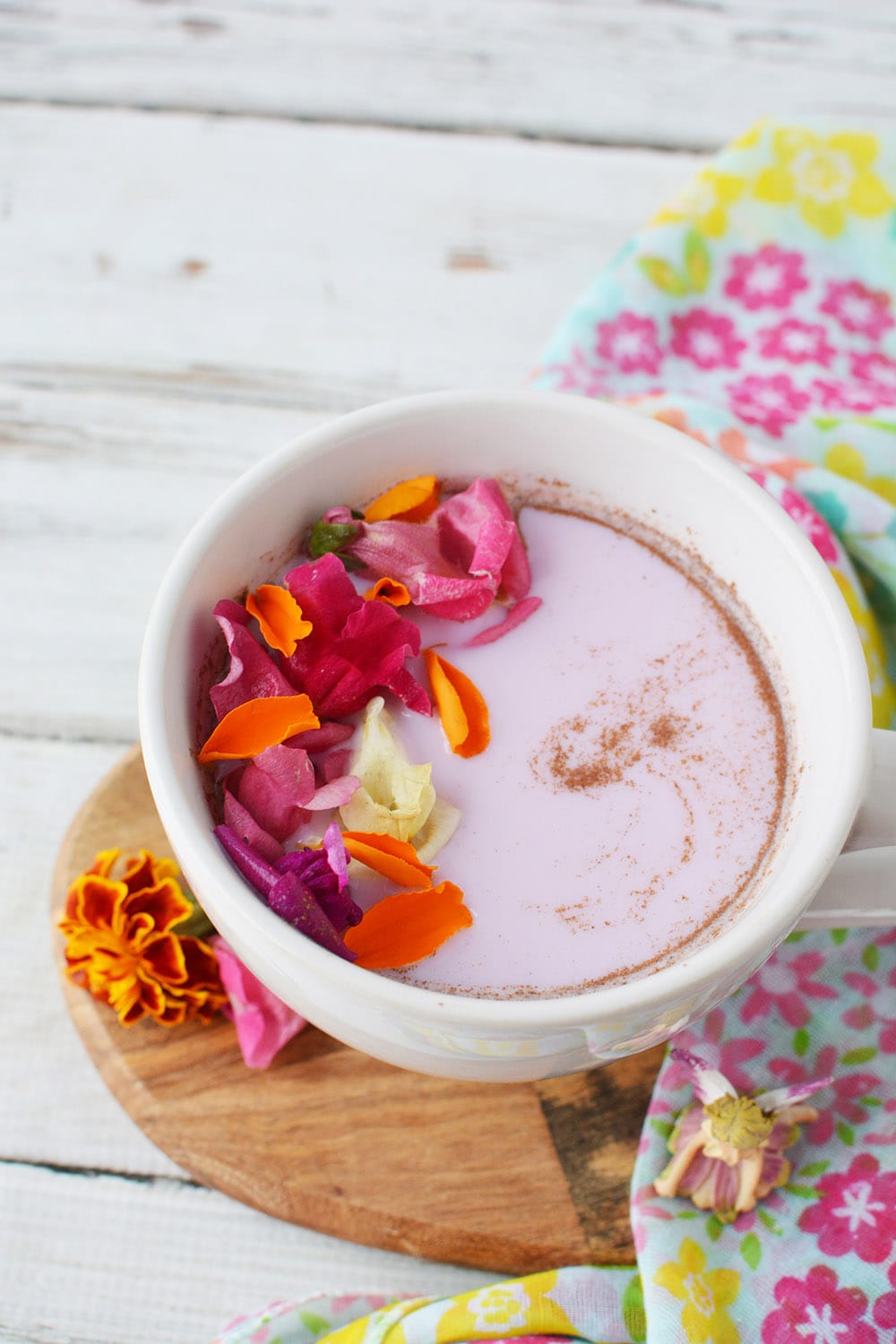 Pink milk in a mug topped with flowers and swirls of cinnamon on a table.