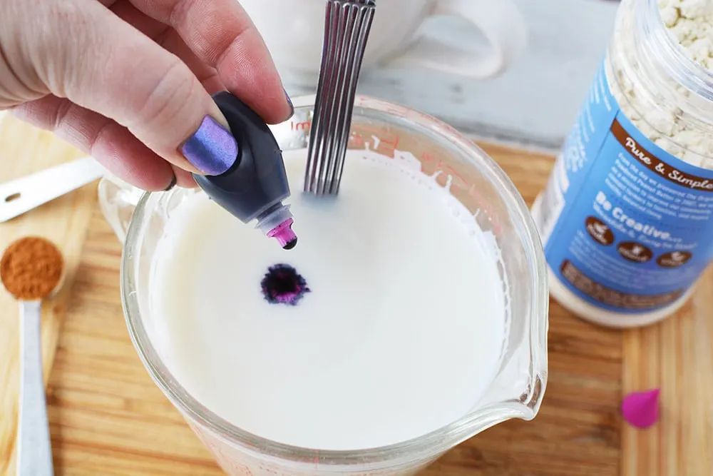Dropping purple food coloring into a glass of milk. 