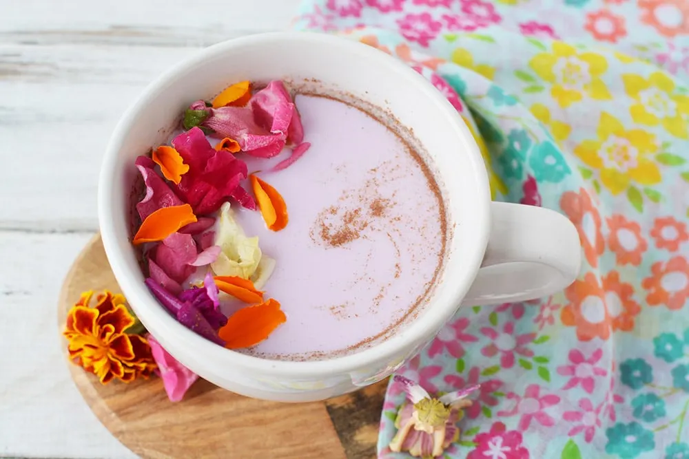 Mug of pink moon milk with edible flowers on top.