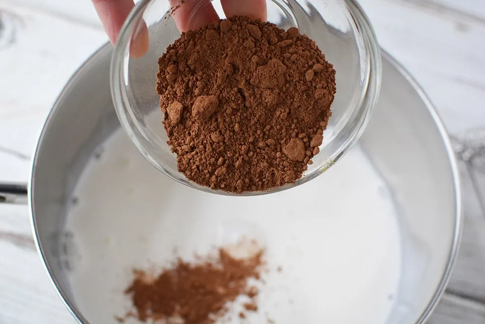 Pouring cocoa into milk in saucepan.