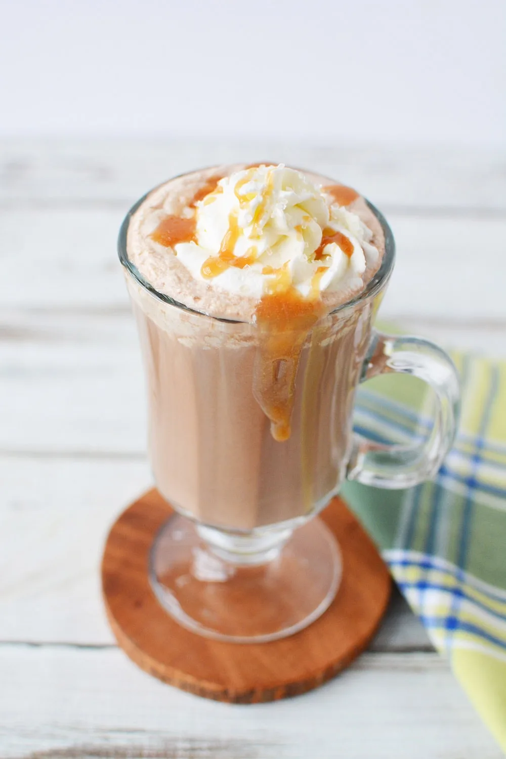 Coffee drink topped with whipped cream and caramel in a glass mug.