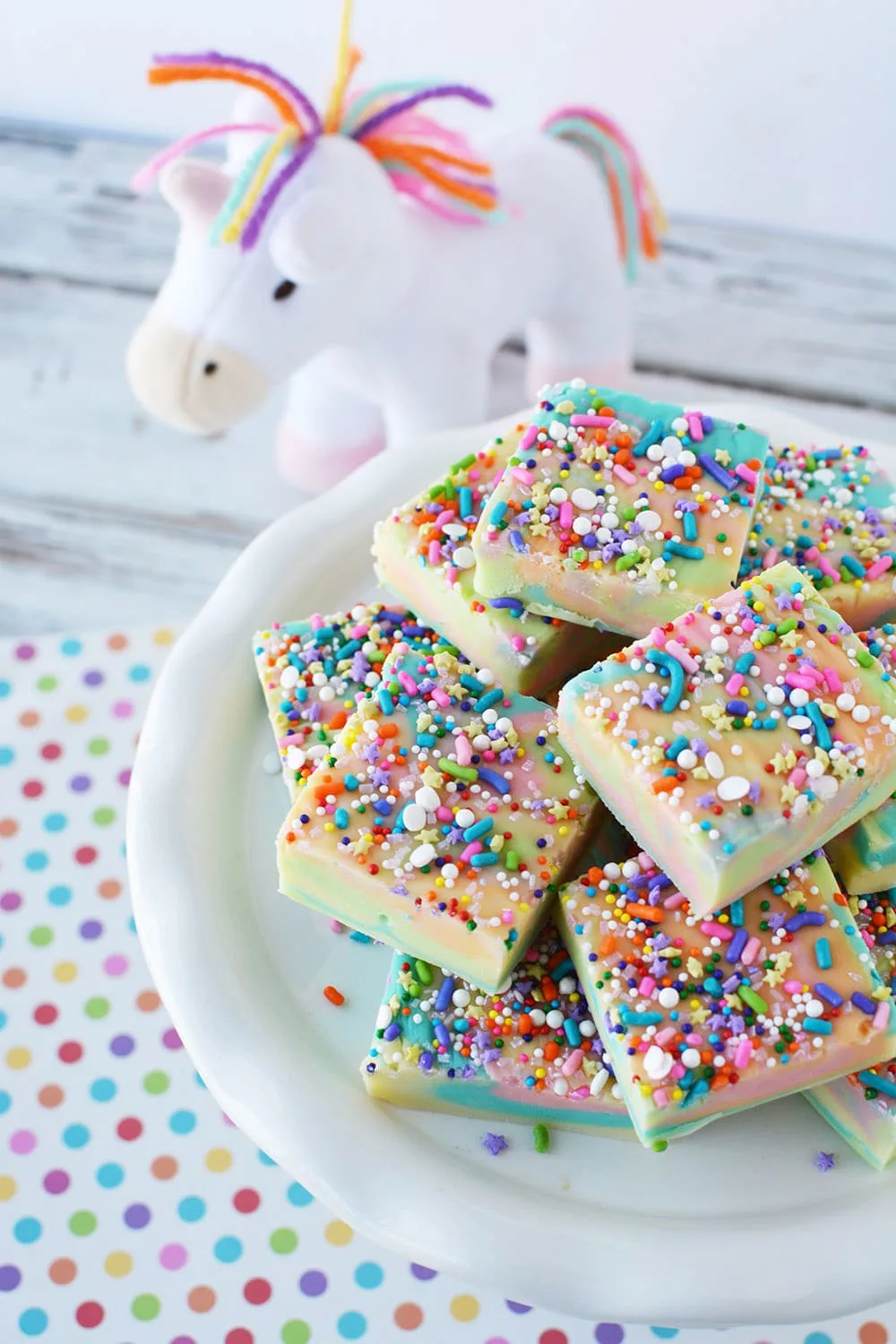 Unicorn fudge on a plate with a unicorn plush toy on the table.