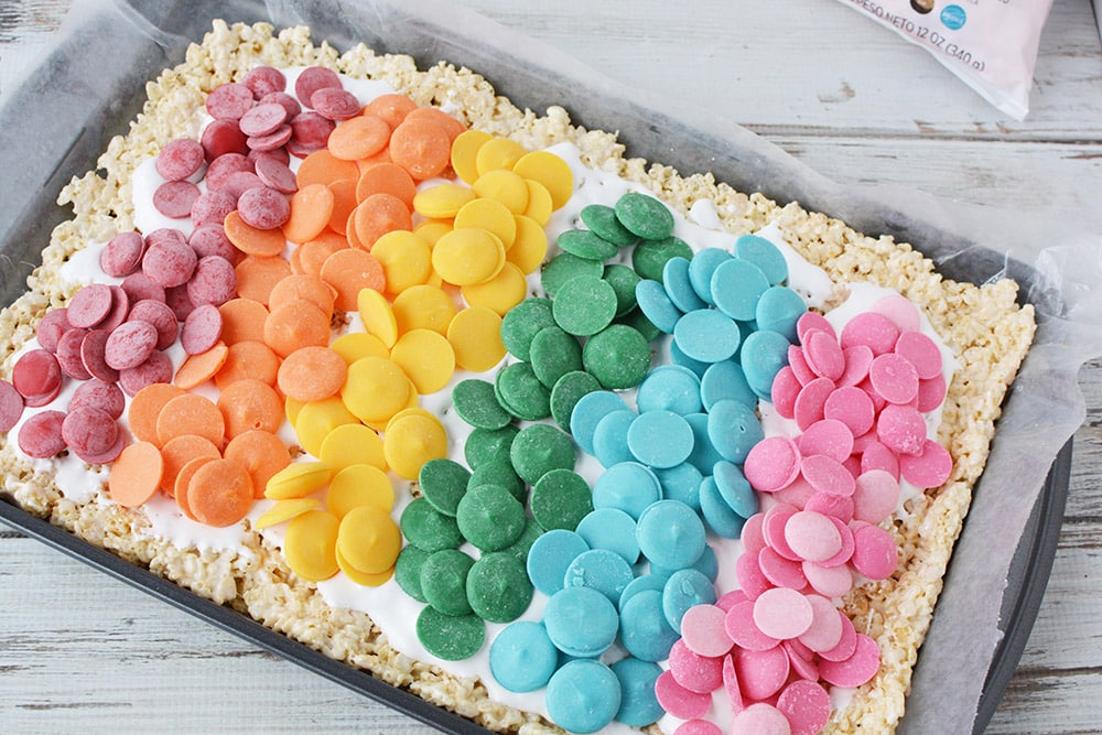 Rainbow of candy melts on top of rice cereal in a baking sheet. 