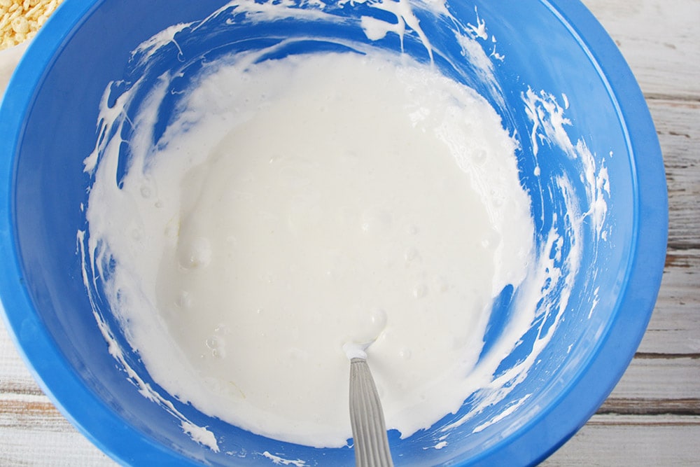 Melted marshmallows in a blue bowl with a spoon. 