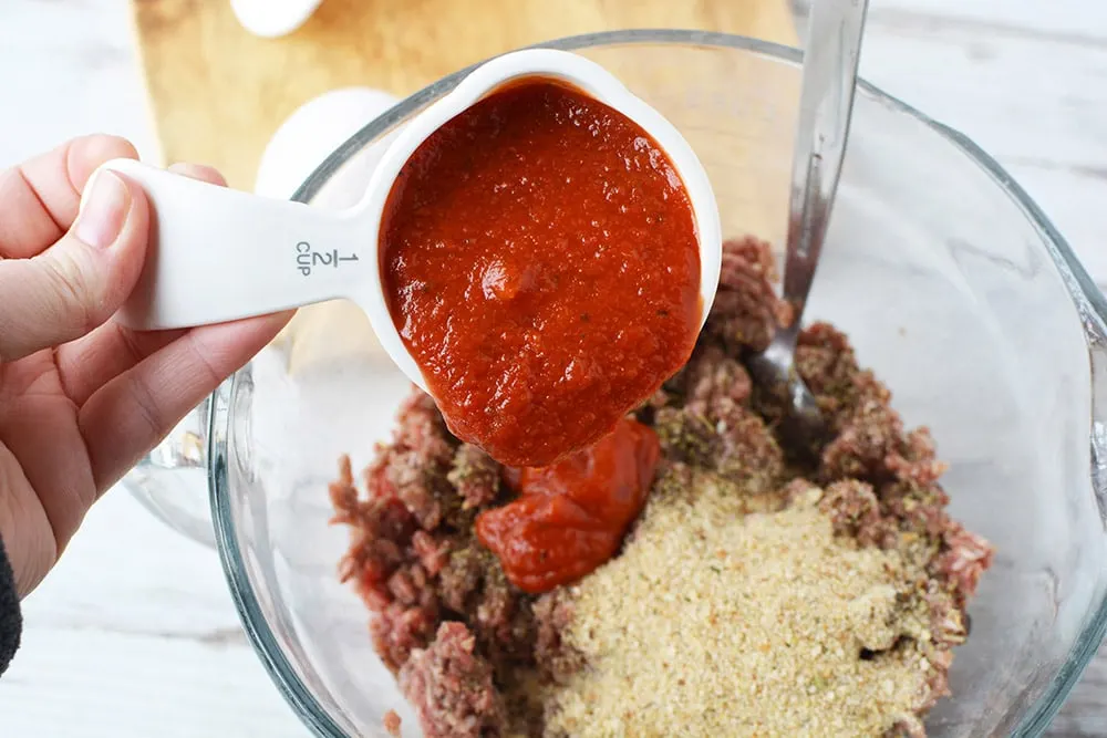 Adding 1/2 cup of pasta sauce into ground beef mixture. 