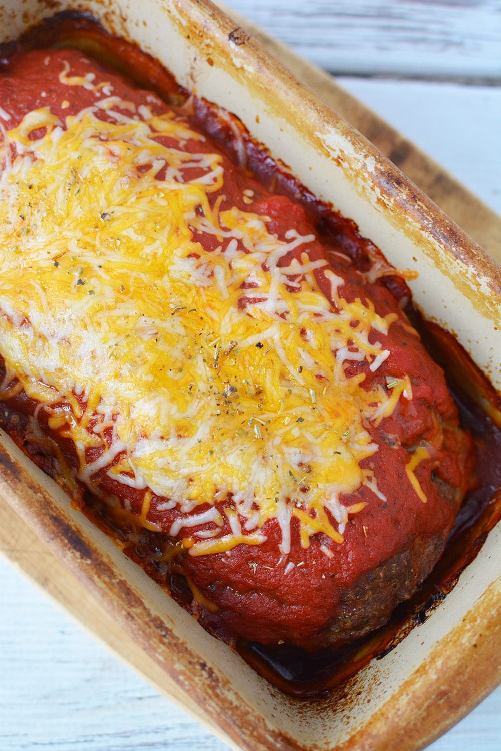 Cheese and sauce on baked meatloaf in a pan.
