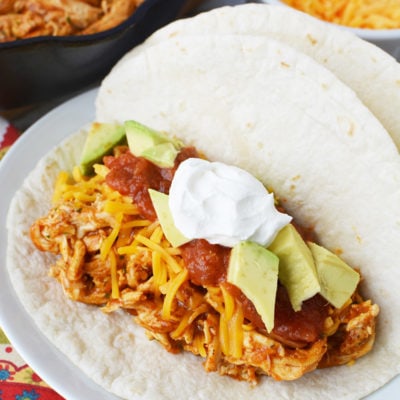 A plate of shredded chicken tacos with ranch and toppings
