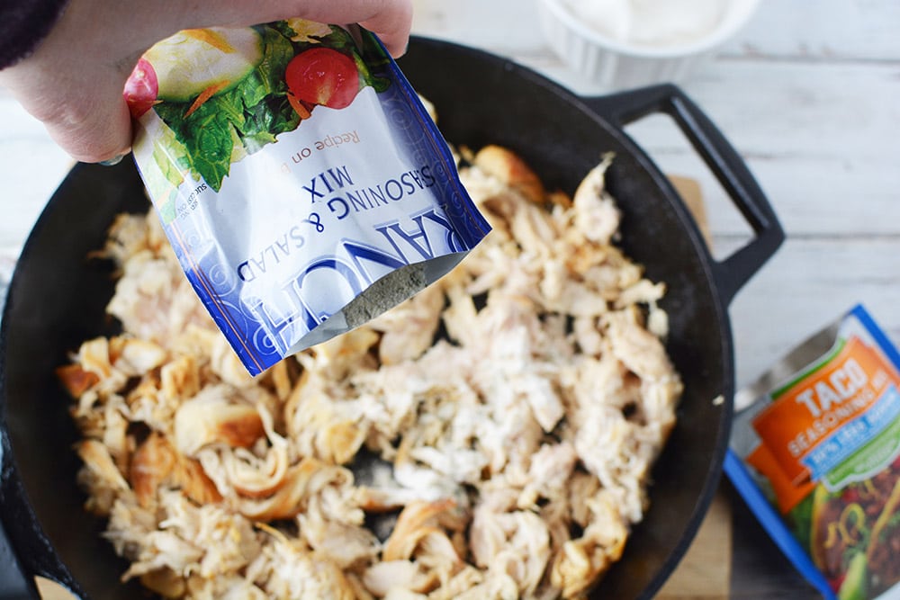 Dumping a packet of ranch dressing mix into shredded chicken. 