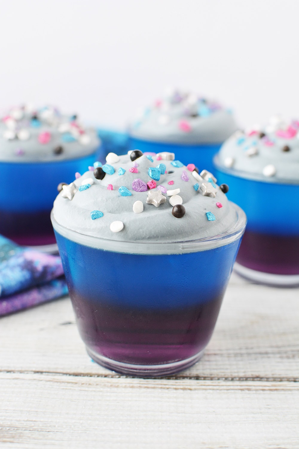 Layered jello topped with gray whipped cream and galaxy sprinkles.