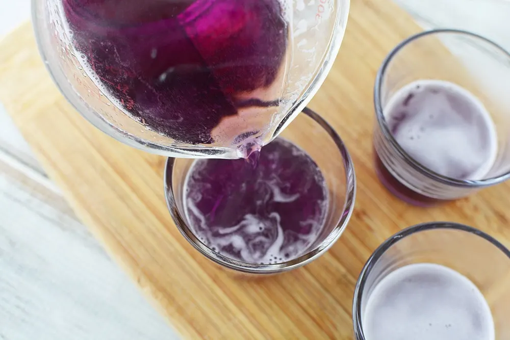 Pouring liquid grape jello into a cup. 