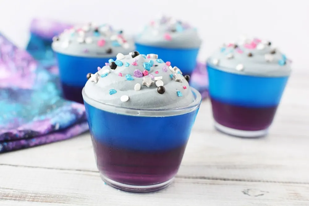 Purple and blue jello cups with gray frosting and sprinkles.