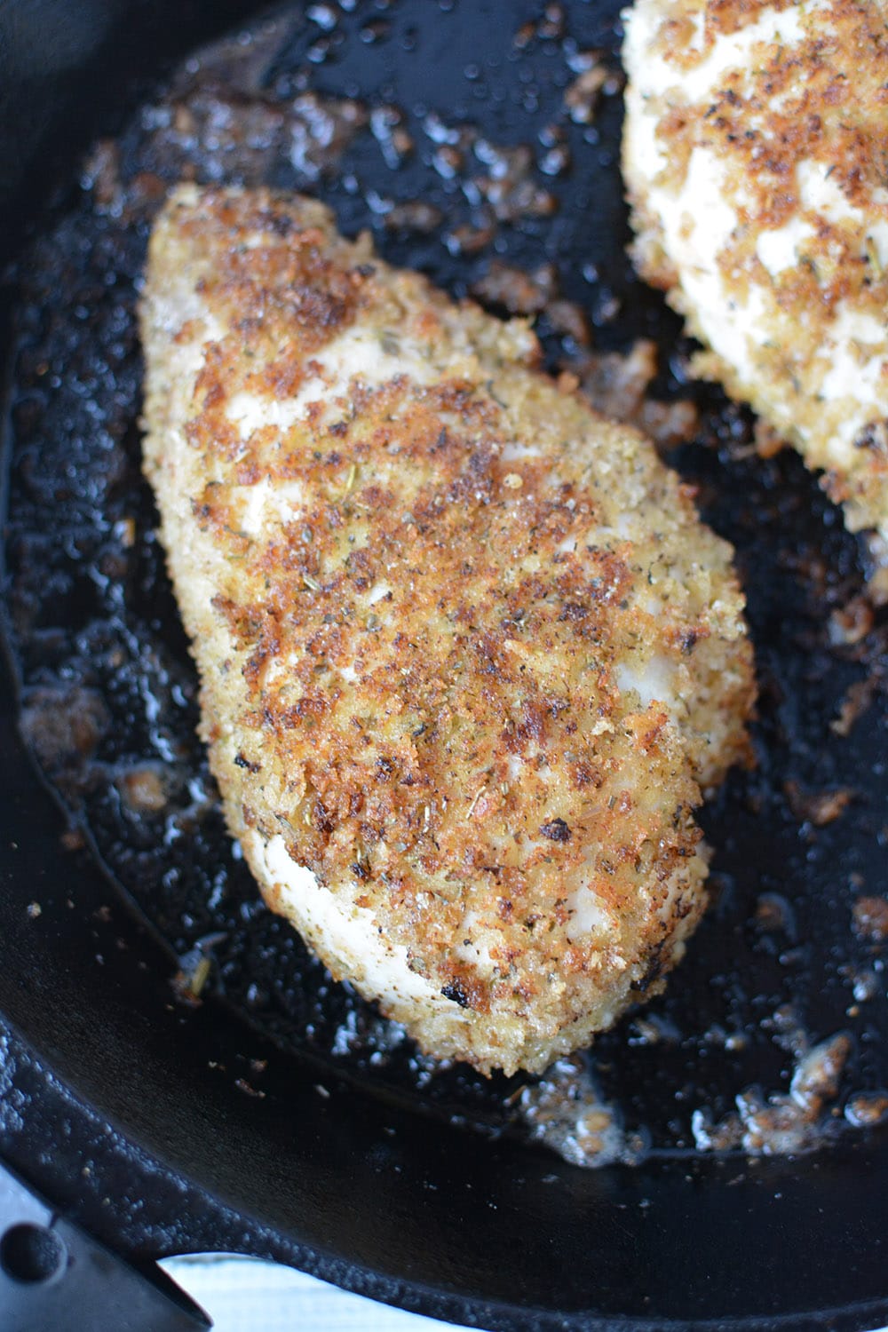 Chicken coated with bread crumbs frying in pan.