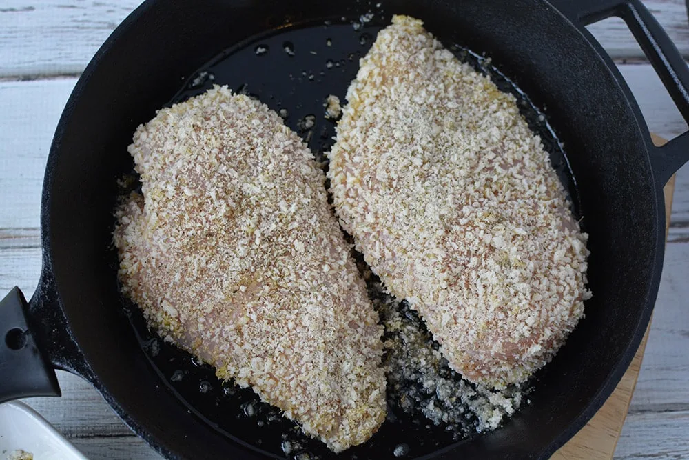 Parmesan crusted chicken breasts in a skillet frying. 