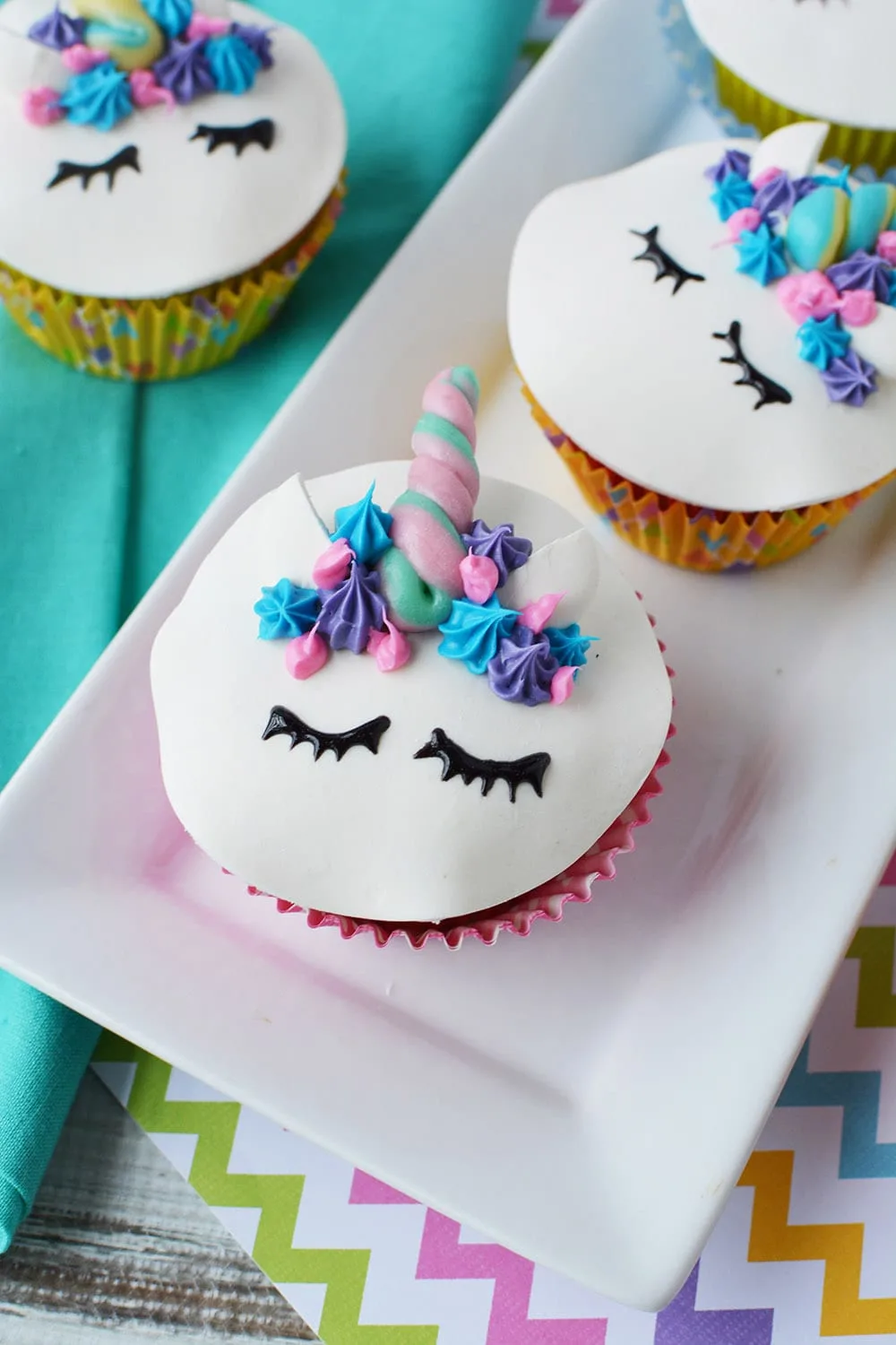 Unicorn cupcakes with eyes, ears, and horns sitting on a tray on a table. 