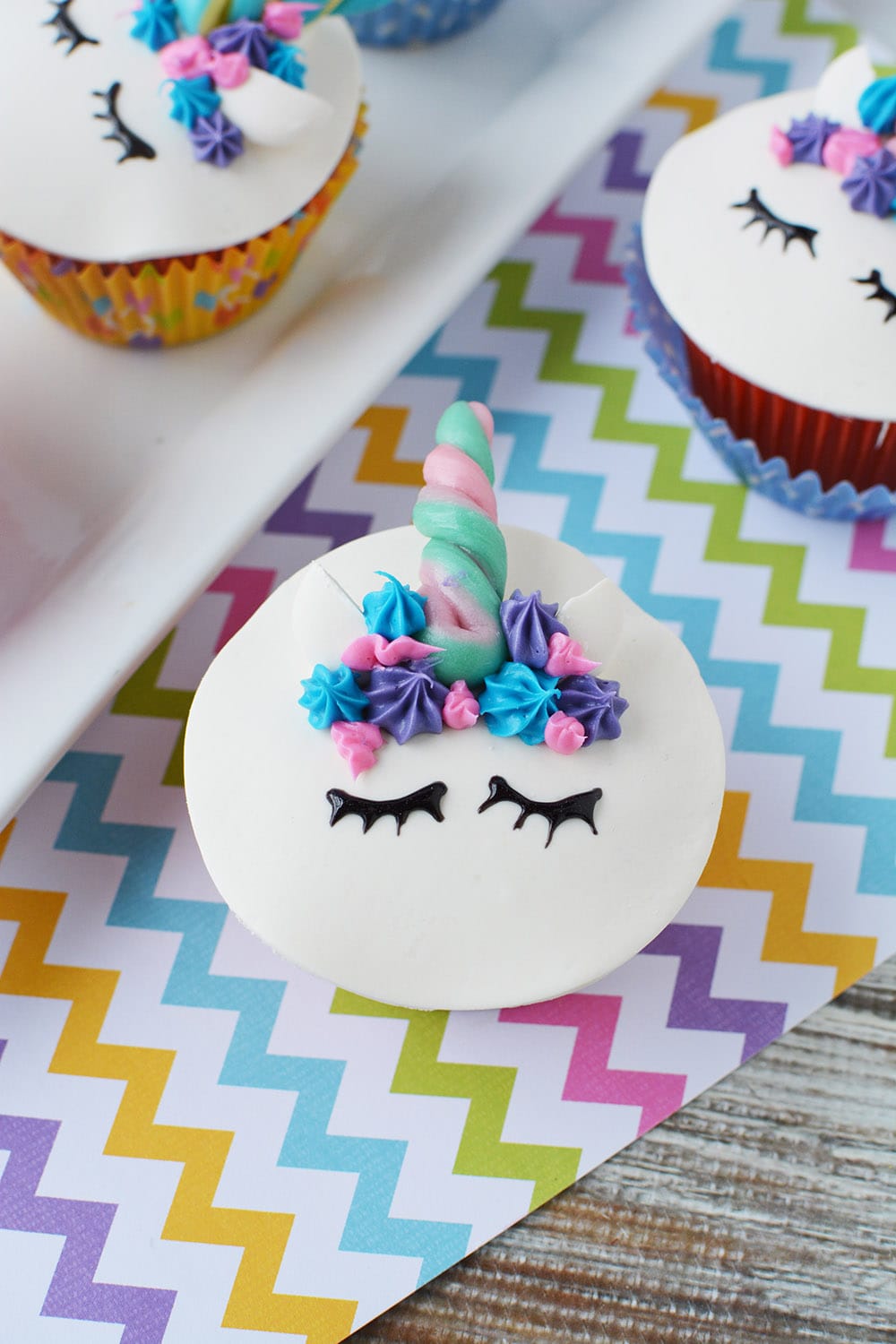 A unicorn cupcake with ears, a candy horn, a frosting mane, and eyes. 