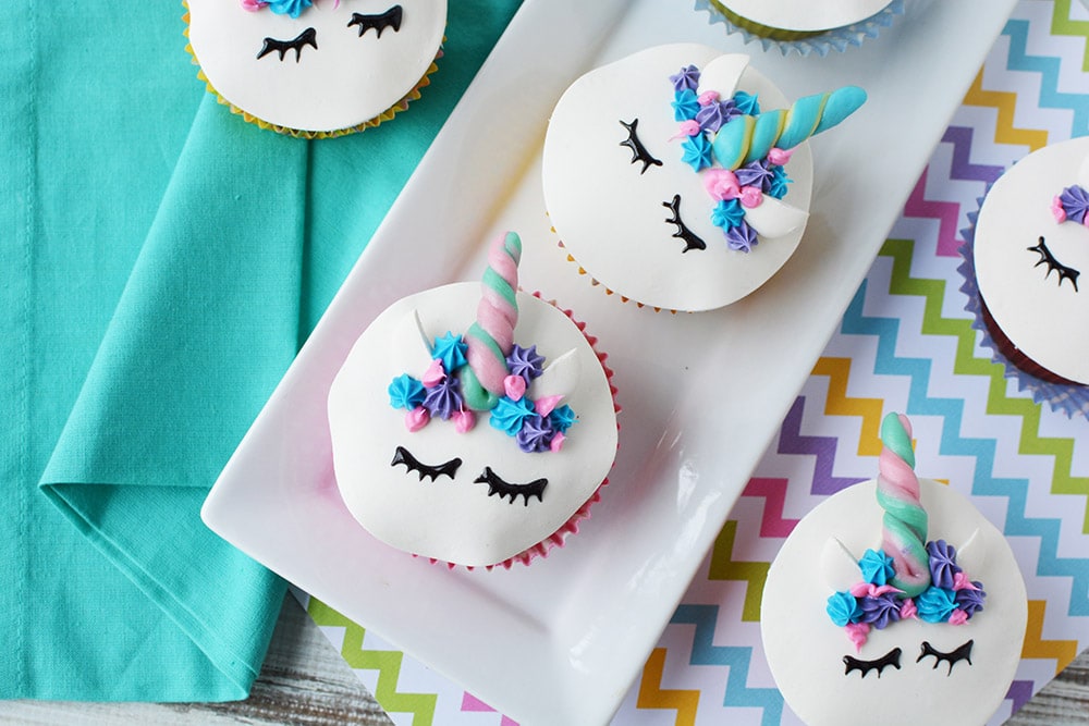 Unicorn cupcakes with faces and horns on a table.