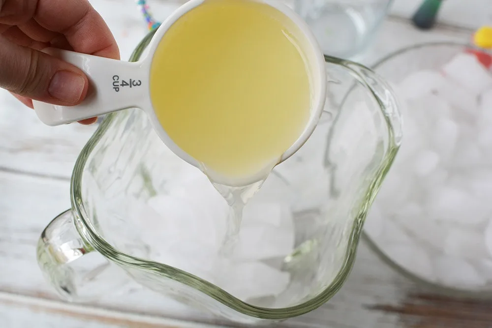 Pouring 3/4 cup of lemonade into a blender with ice in it. 