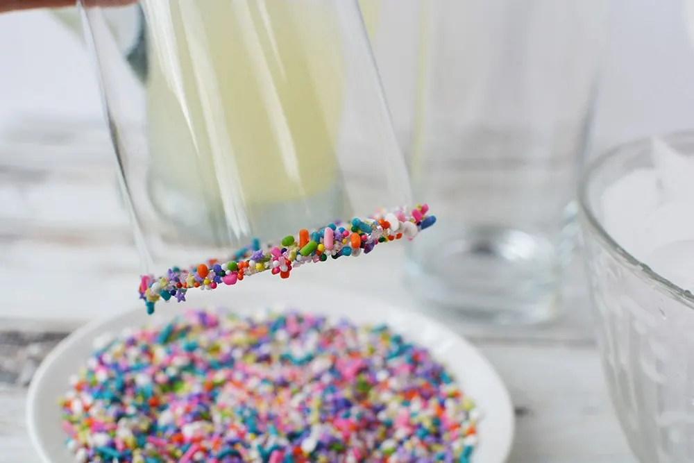 Sprinkles around the lip of a glass above the plate of sprinkles. 