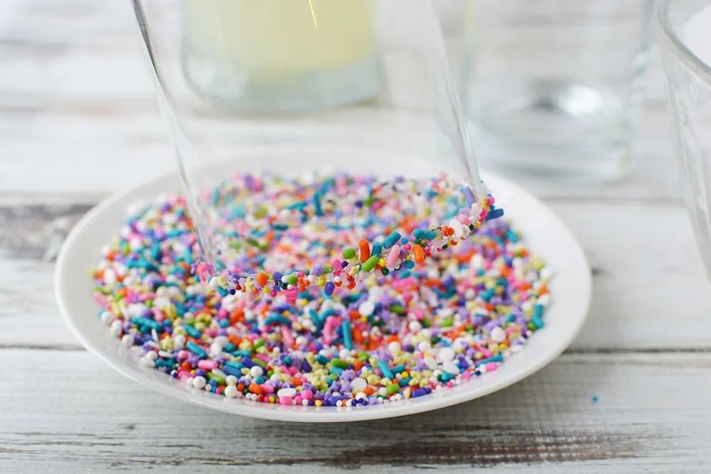 Dipping a glass into rainbow sprinkles on a plate. 