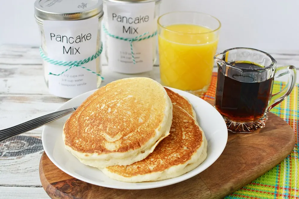 Pancakes on a plate with jars of homemade pancake mix, orange juice, and syrup. 
