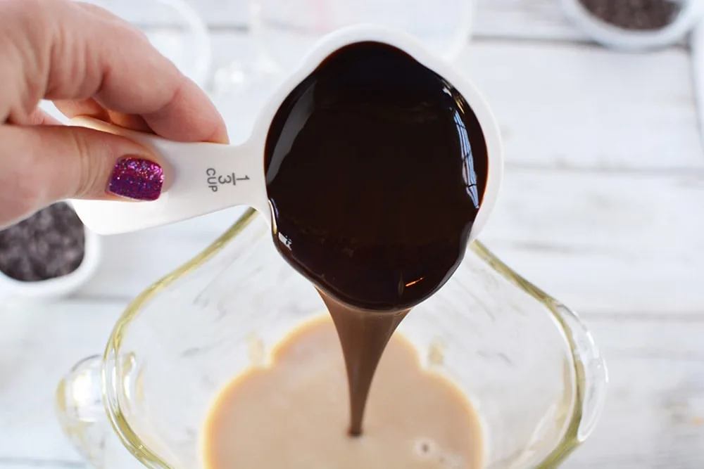 Dumping syrup into coffee mixture in a blender. 