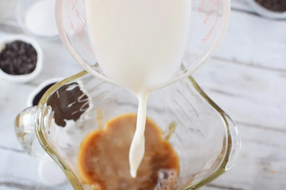 Pouring milk into coffee that's in a blender. 