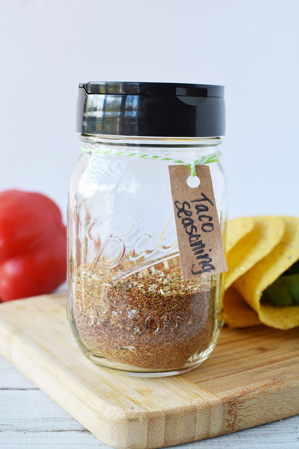 Jar of taco seasoning mix by a red pepper and taco shells. 