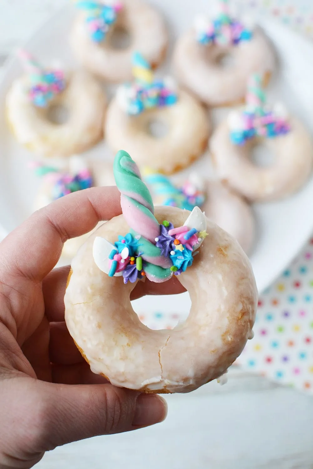 Holding up a unicorn donut with full plate in the background.
