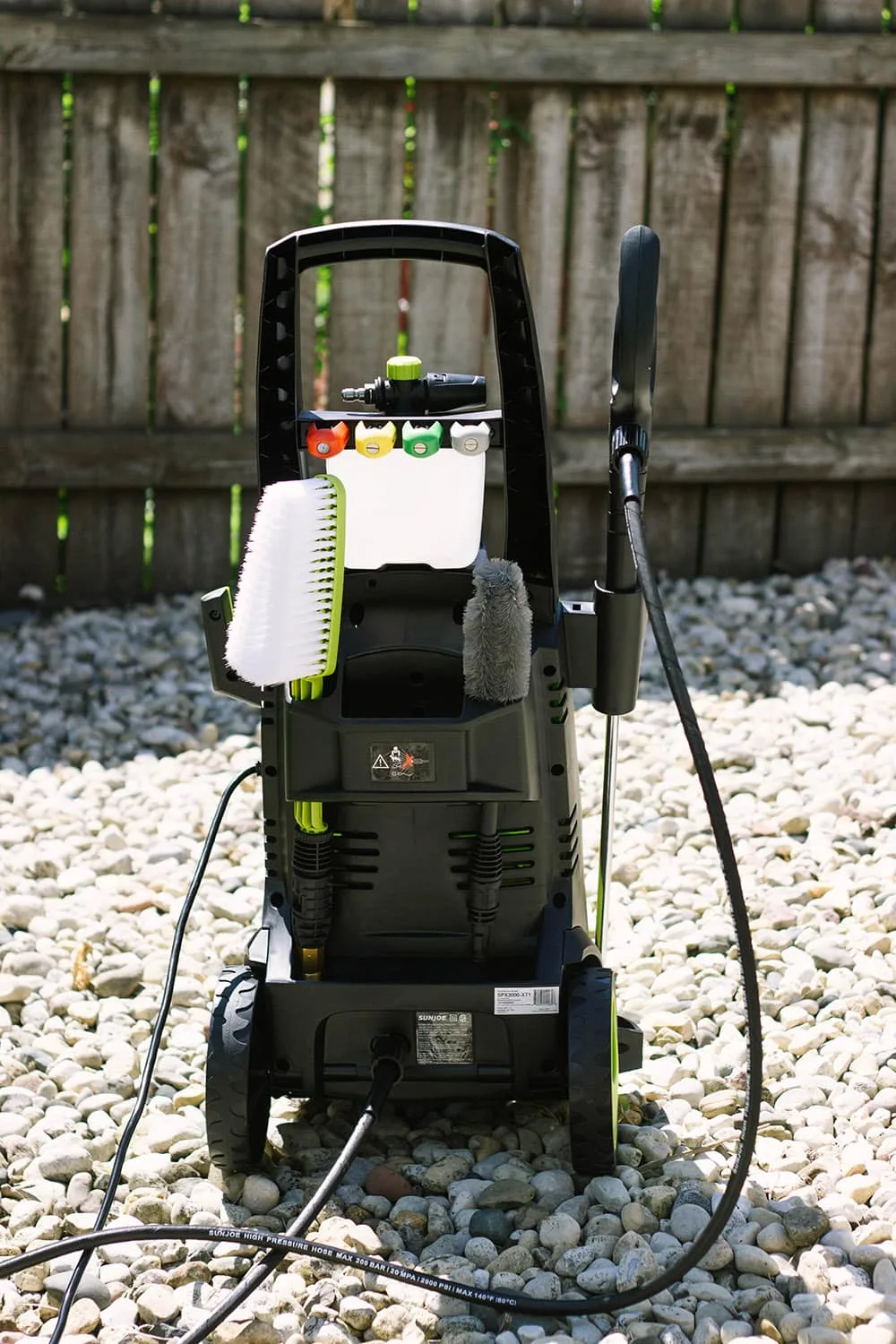 Back of the power washer on rocks near a fence. 