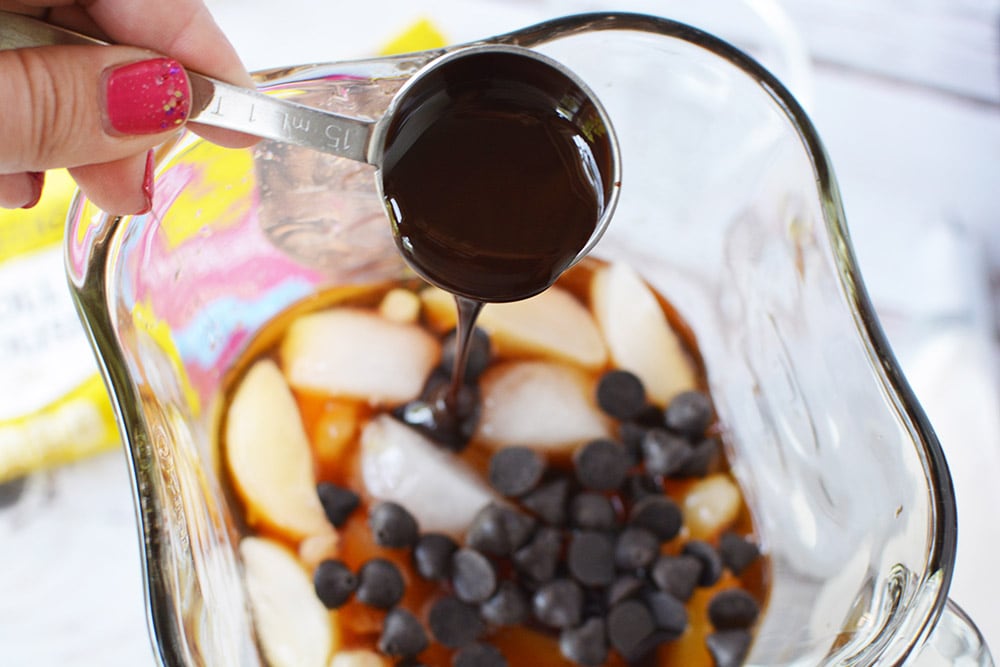 Pouring syrup into a blender on top of ice and chips. 