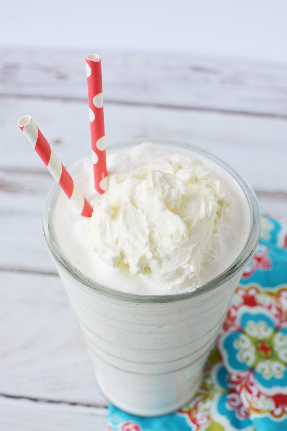 Blended vanilla bean frappe in a glass with two red straws.