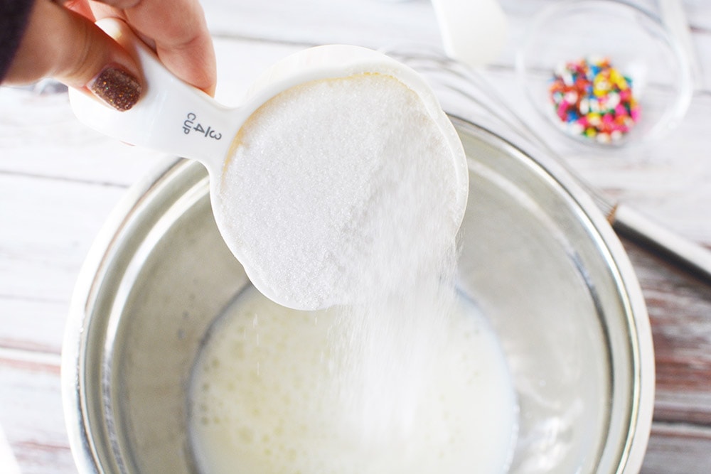 Adding sugar to a bowl on top of milk.