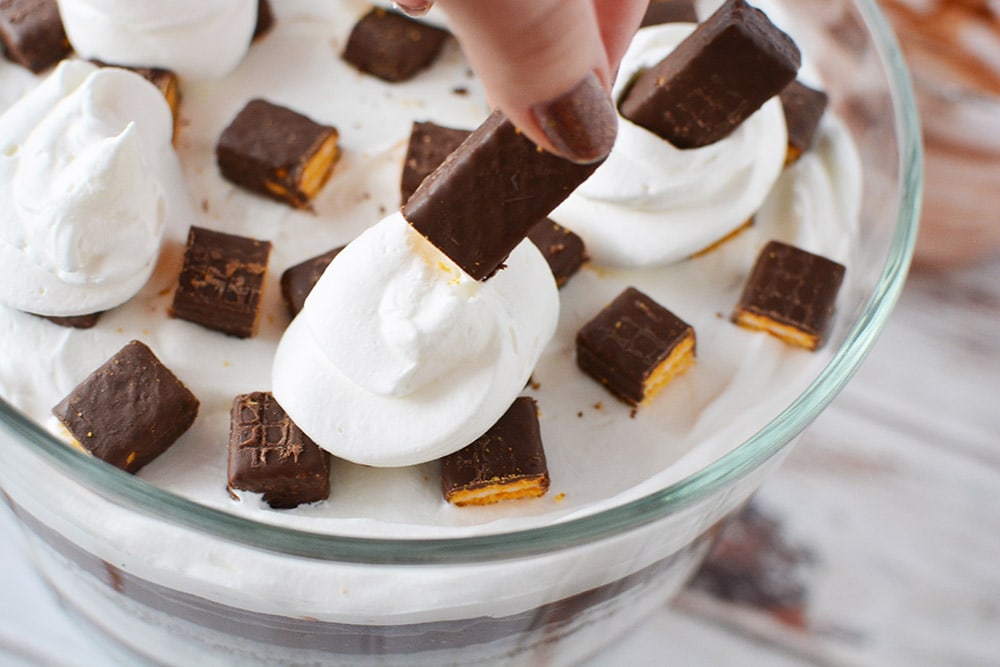 Adding fudge sticks to dollops of whipped topping in a trifle bowl. 