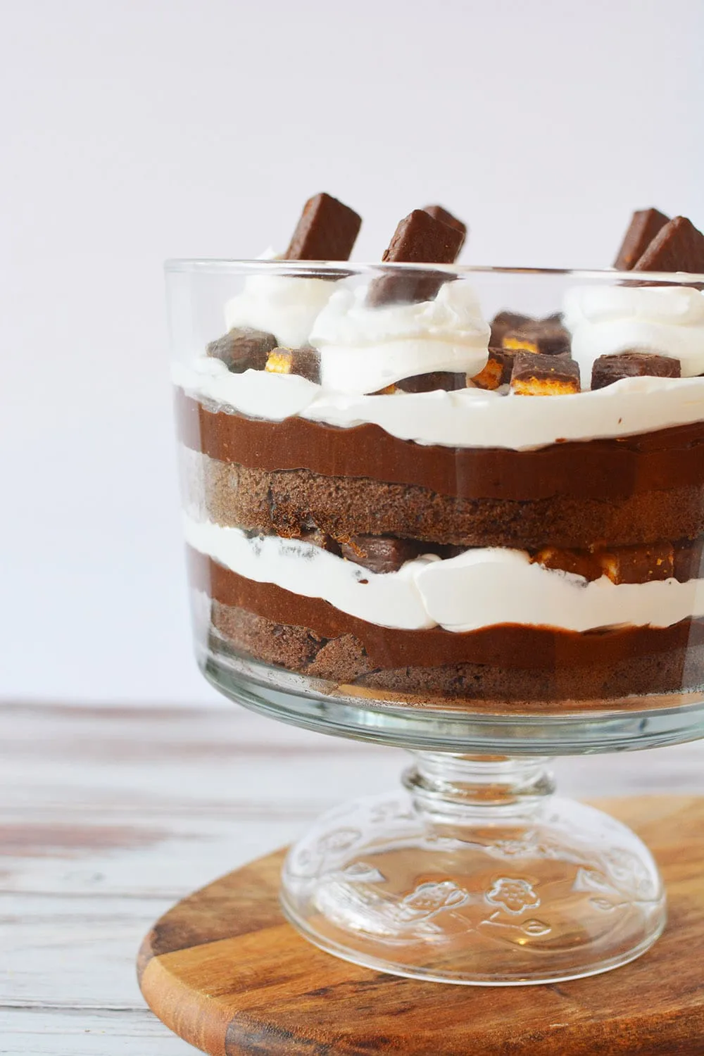 Chocolate trifle with layers of pudding, whipped cream, and cake in a bowl sitting on top of a cutting board. 