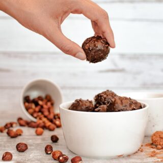 holding a date ball above other coconut balls and hazelnuts in the background