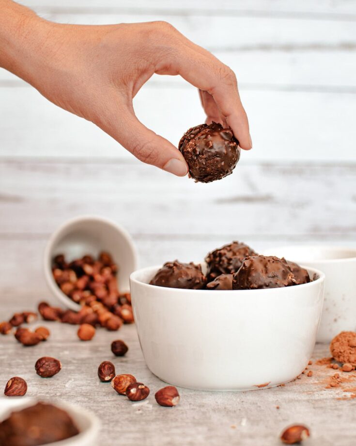 holding a date ball above other coconut balls and hazelnuts in the background