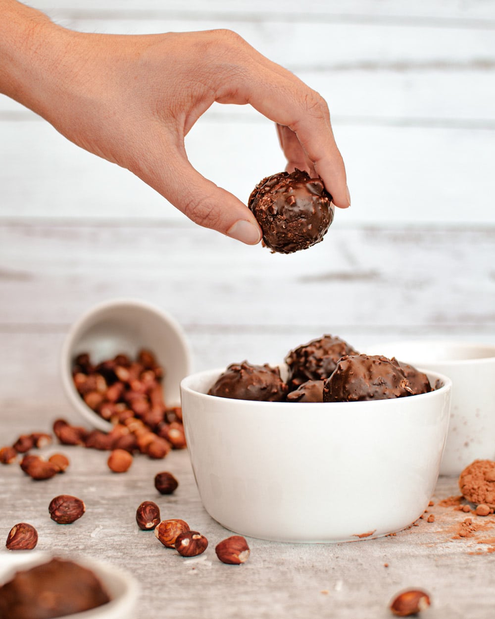 Holding a date ball above other coconut balls and hazelnuts in the background.