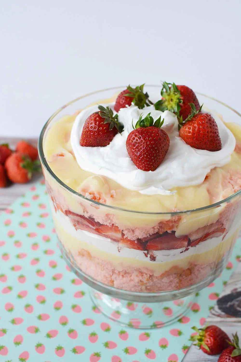 Layers of strawberry cake, cheesecake pudding, whipped cream, and strawberries in a trifle bowl