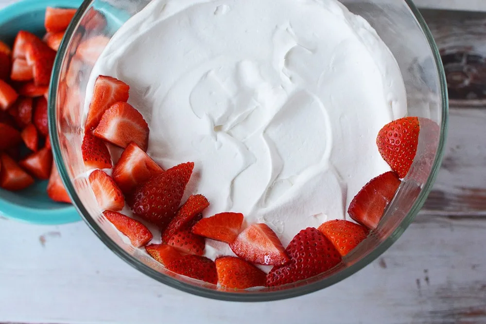 Fresh strawberries on top of whipped cream in a trifle bowl.
