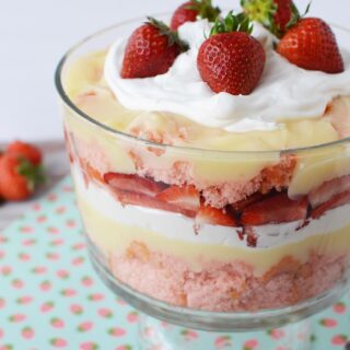 A trifle bowl with layers of cake, strawberries, pudding, and whipped cream topped with fresh berries