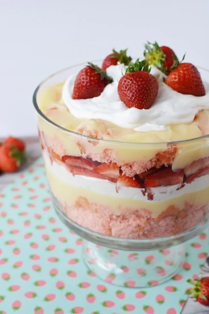 A trifle bowl with layers of cake, strawberries, pudding, and whipped cream topped with fresh berries