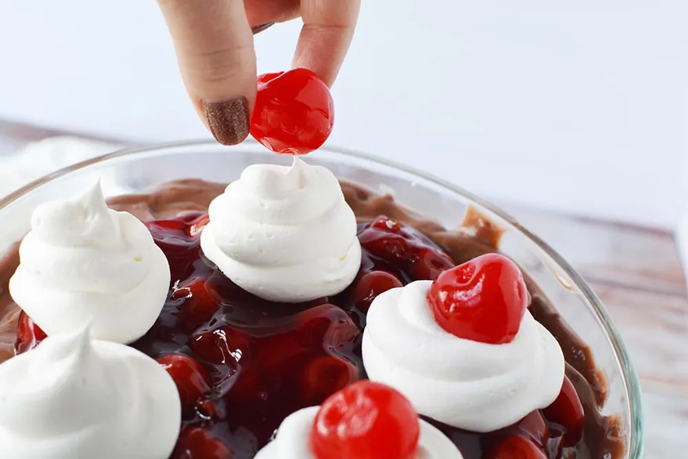 Placing cherries on whipped cream on top of a black forest trifle.