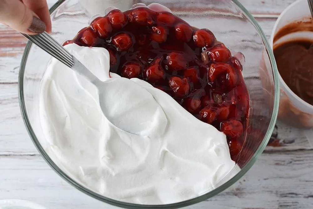 Adding a layer of whipped topping to a cherry trifle.