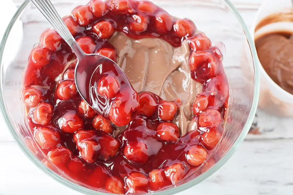 Placing cherry pie filling onto pudding and cake in a trifle.