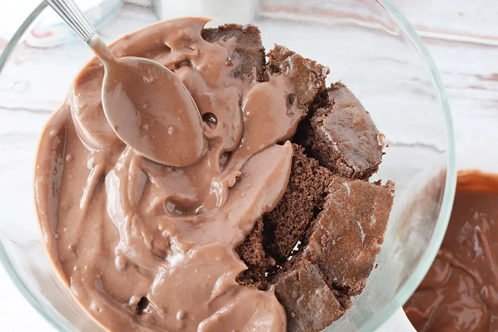 Spooning chocolate pudding onto cake cubes in a trifle dish.