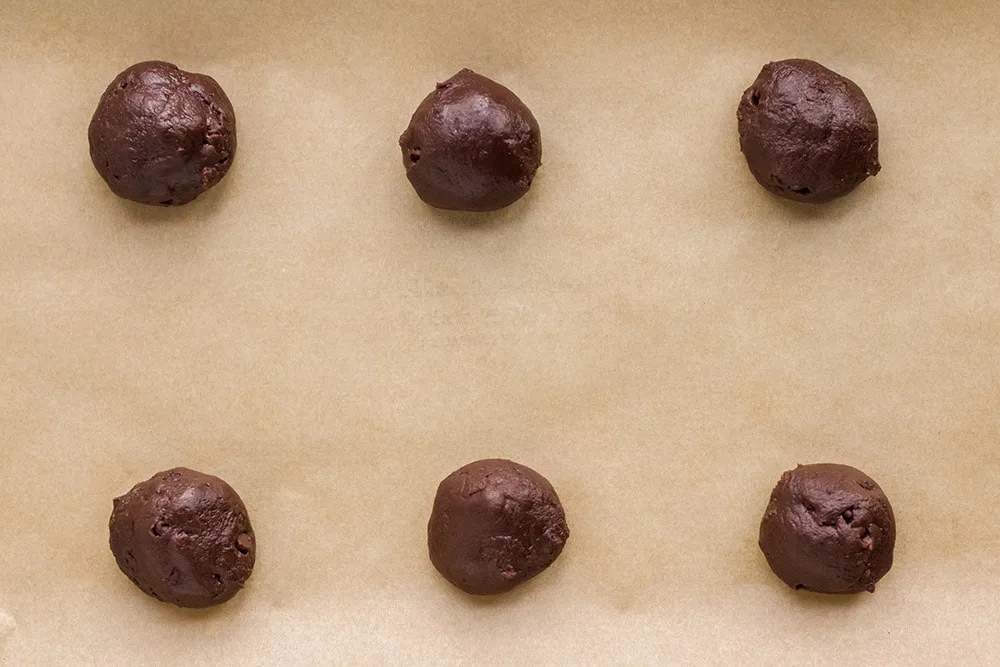 Balls of brownie mix dough on a cookie sheet. 