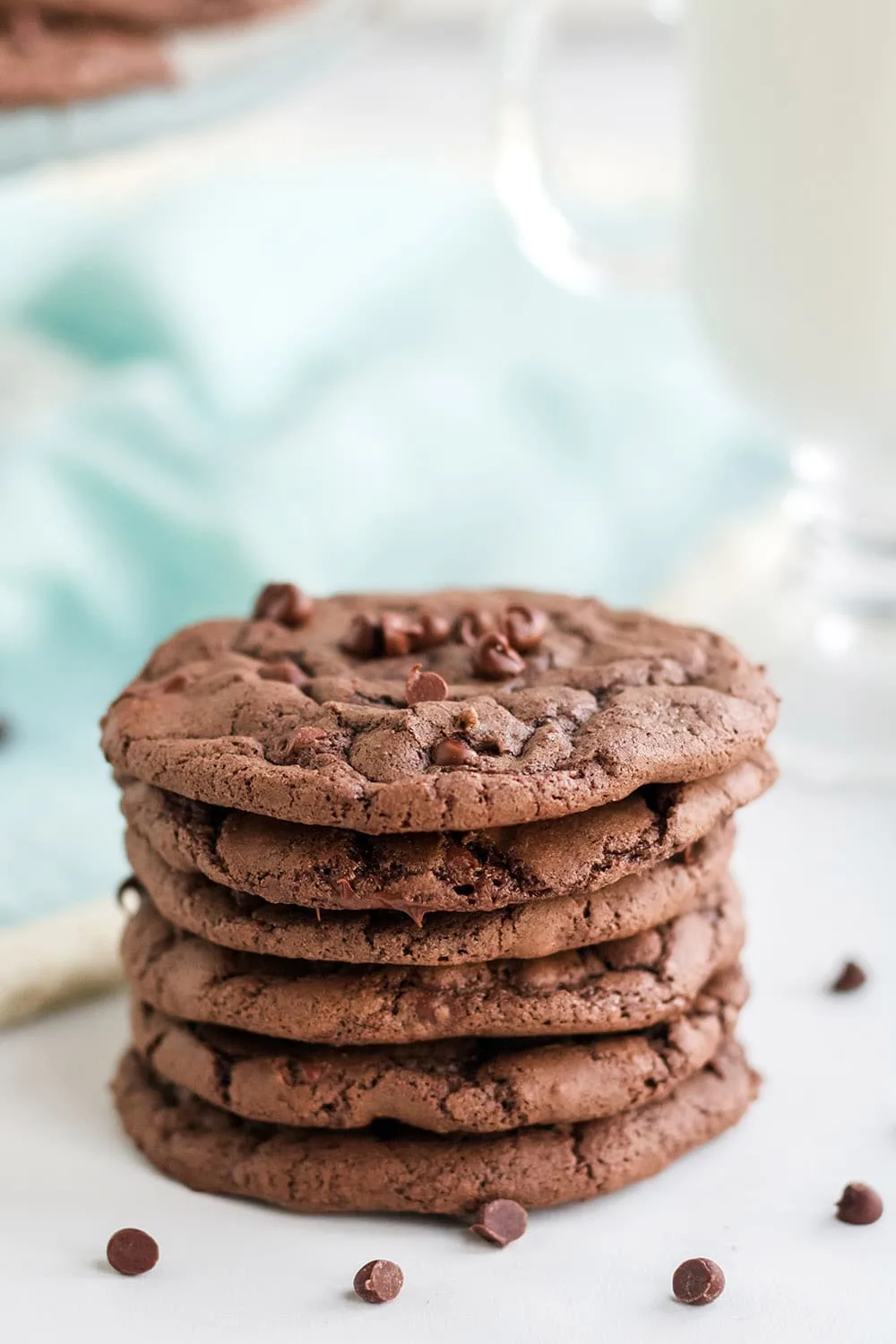 Brownie mix cookies stacked with chocolate chips on a white table with light blue napkin.