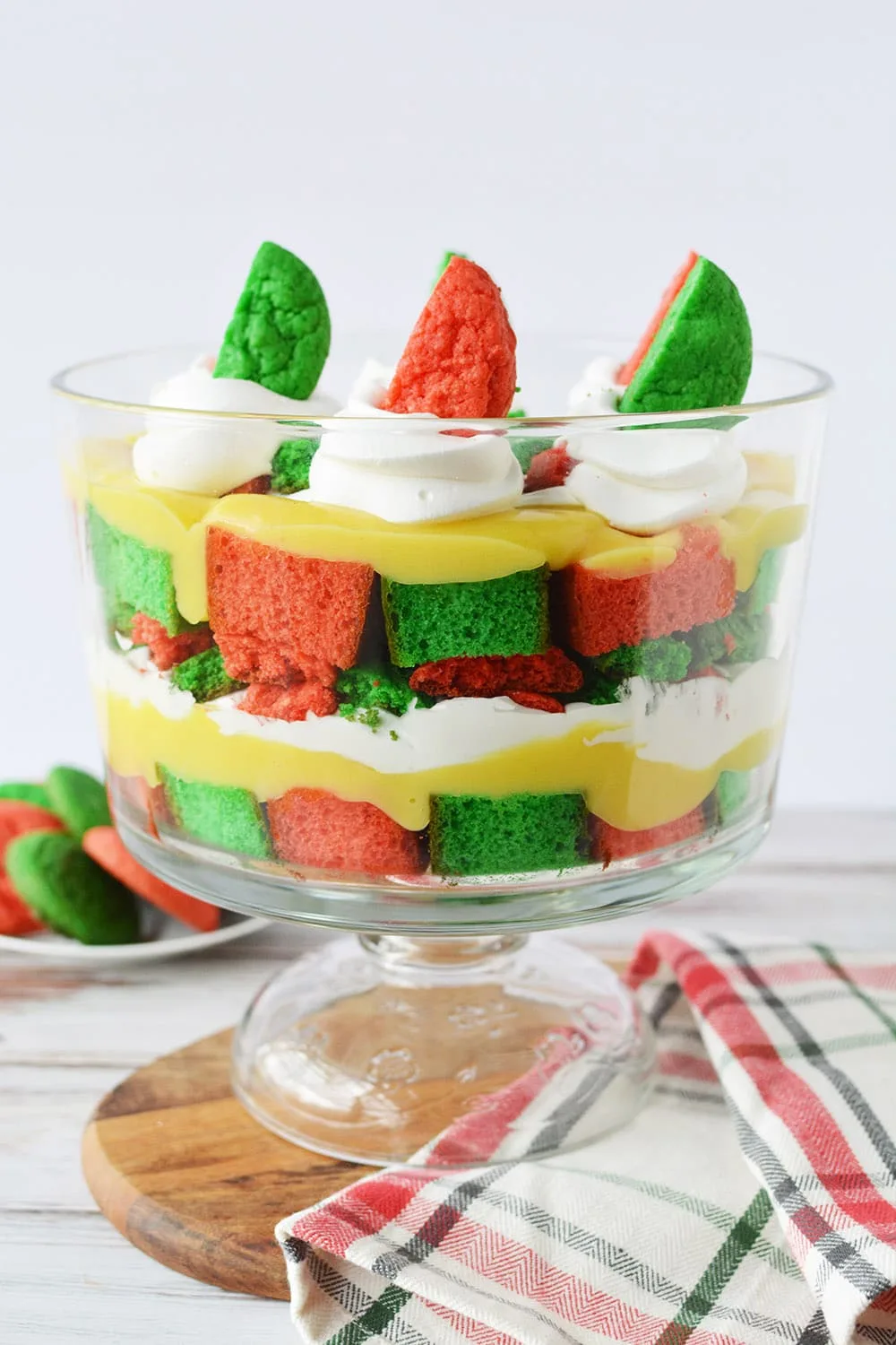 Layers of red and green cake, cookies, whipped cream, and pudding in a trifle dish.