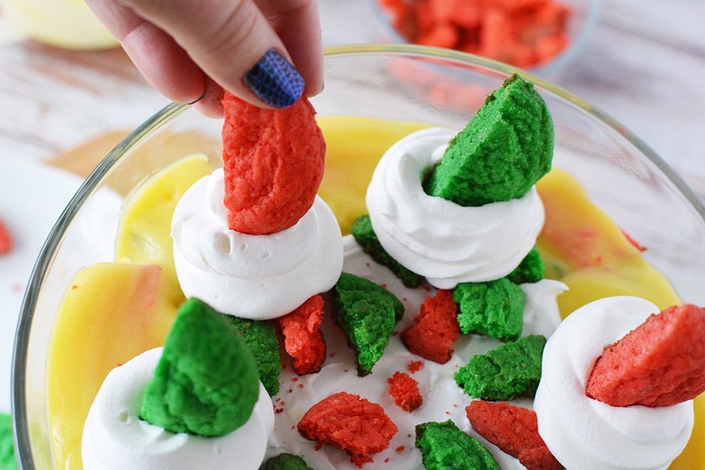 Putting red and green cookies into whipped cream on Christmas trifle.
